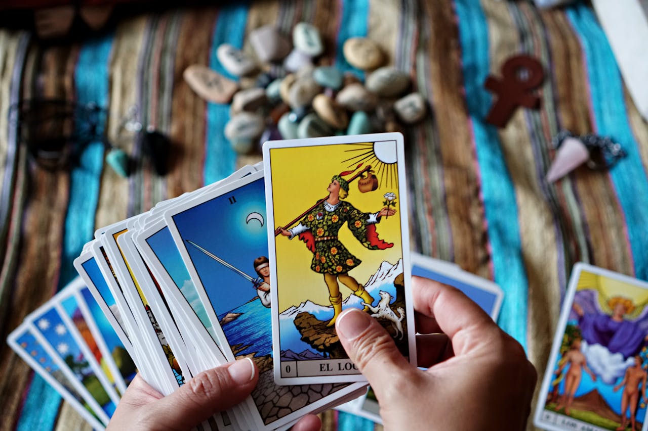 Hands holding tarot cards over a vibrant striped cloth with stones and charms, creating a spiritual atmosphere.